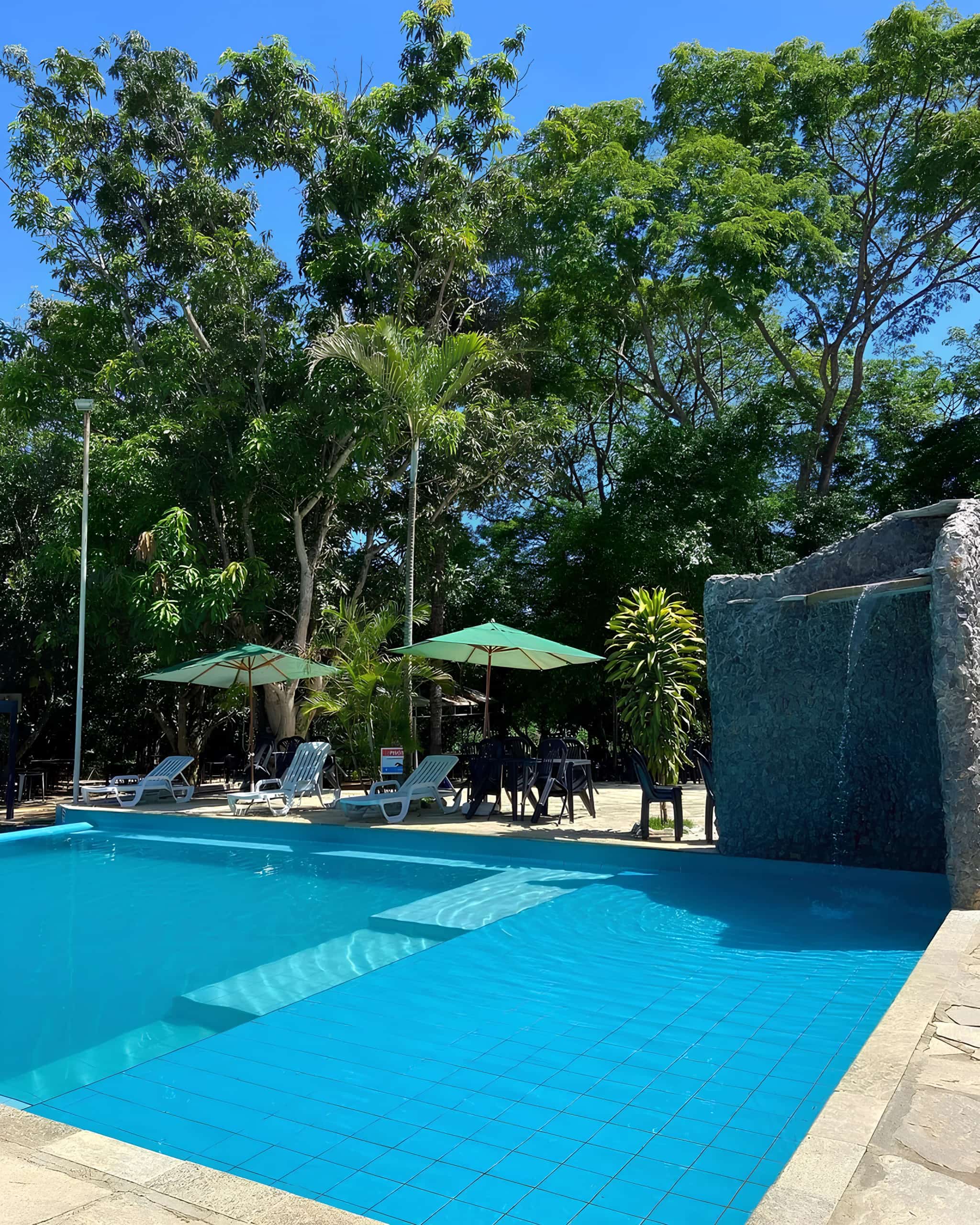 Piscina adulta de água azul com cascata de pedra e guarda-sóis ao redor