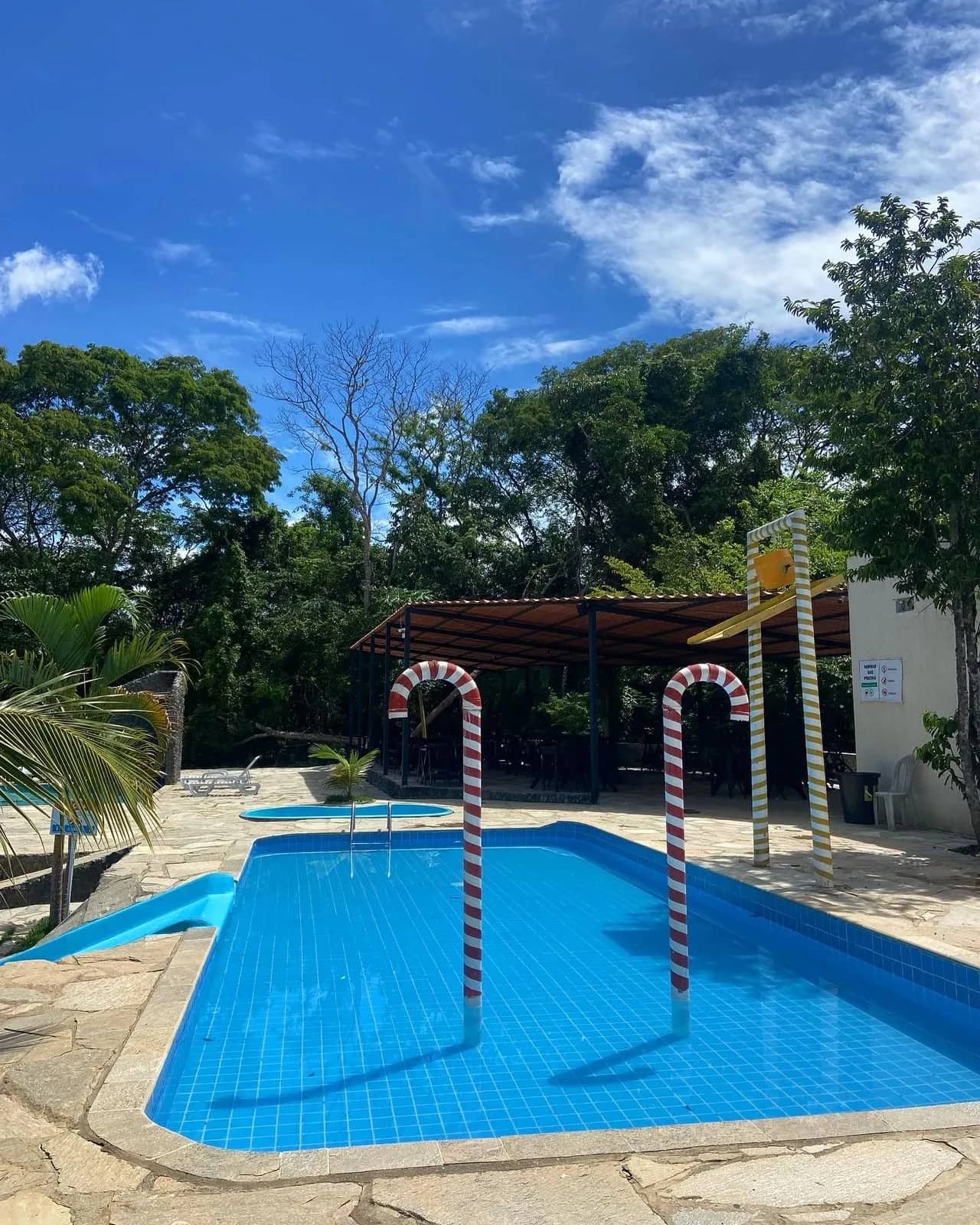Piscina infantil azul com arcos coloridos e ducha sob céu limpo