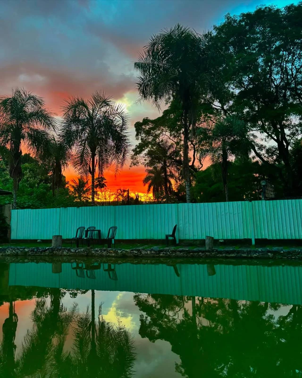 Lagoa refletindo o céu alaranjado do entardecer com cadeiras na margem