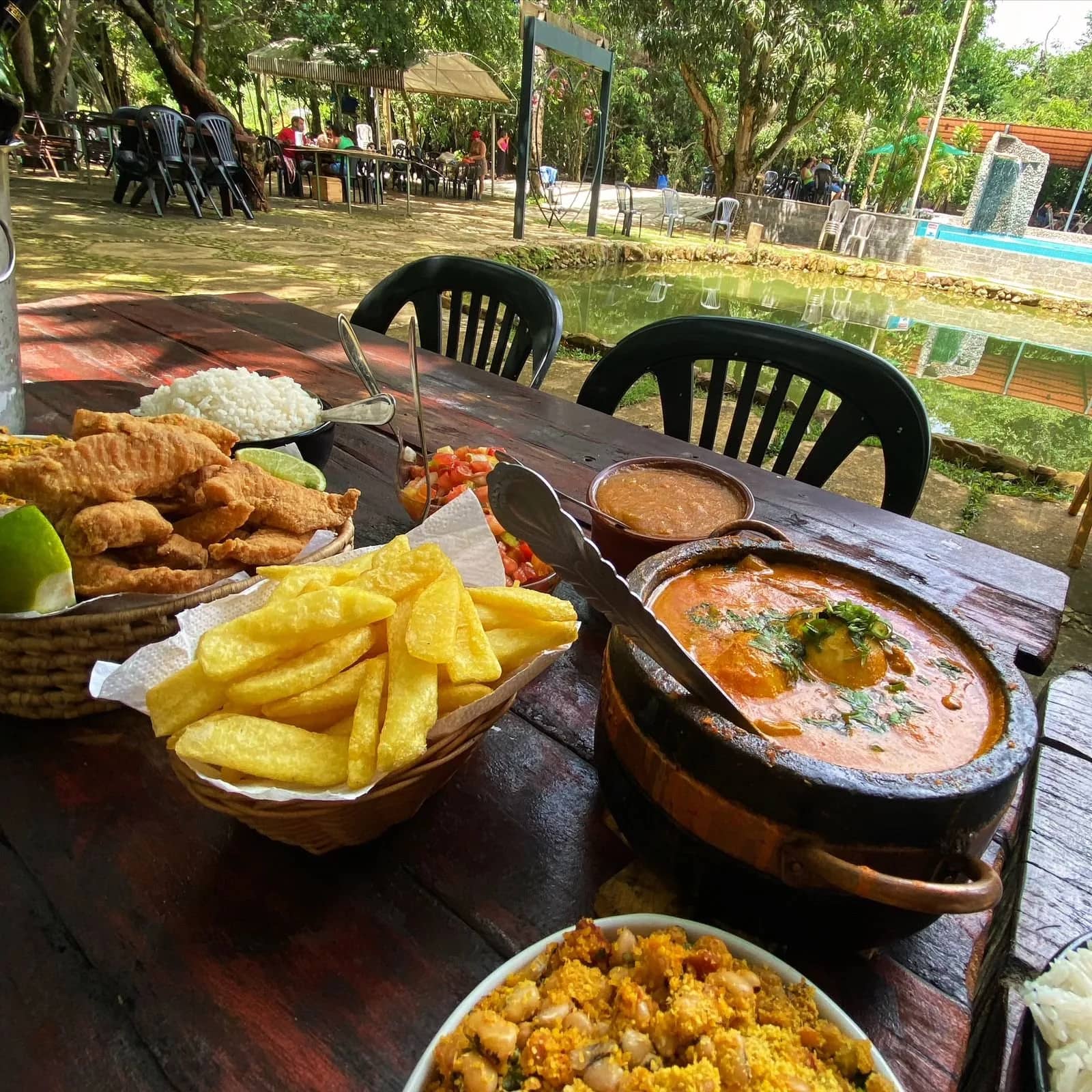 Peixe frito, batata, moqueca e farofa servidos em mesa rústica junto à lagoa