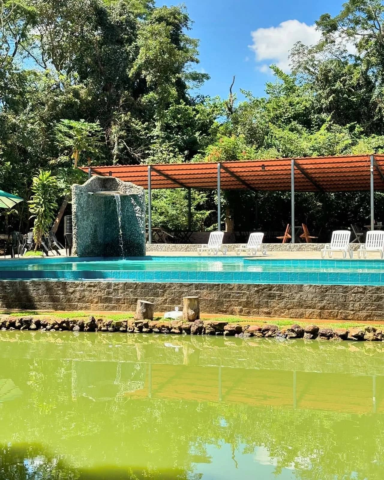 Cascata de pedra despejando água na piscina, com a lagoa em primeiro plano