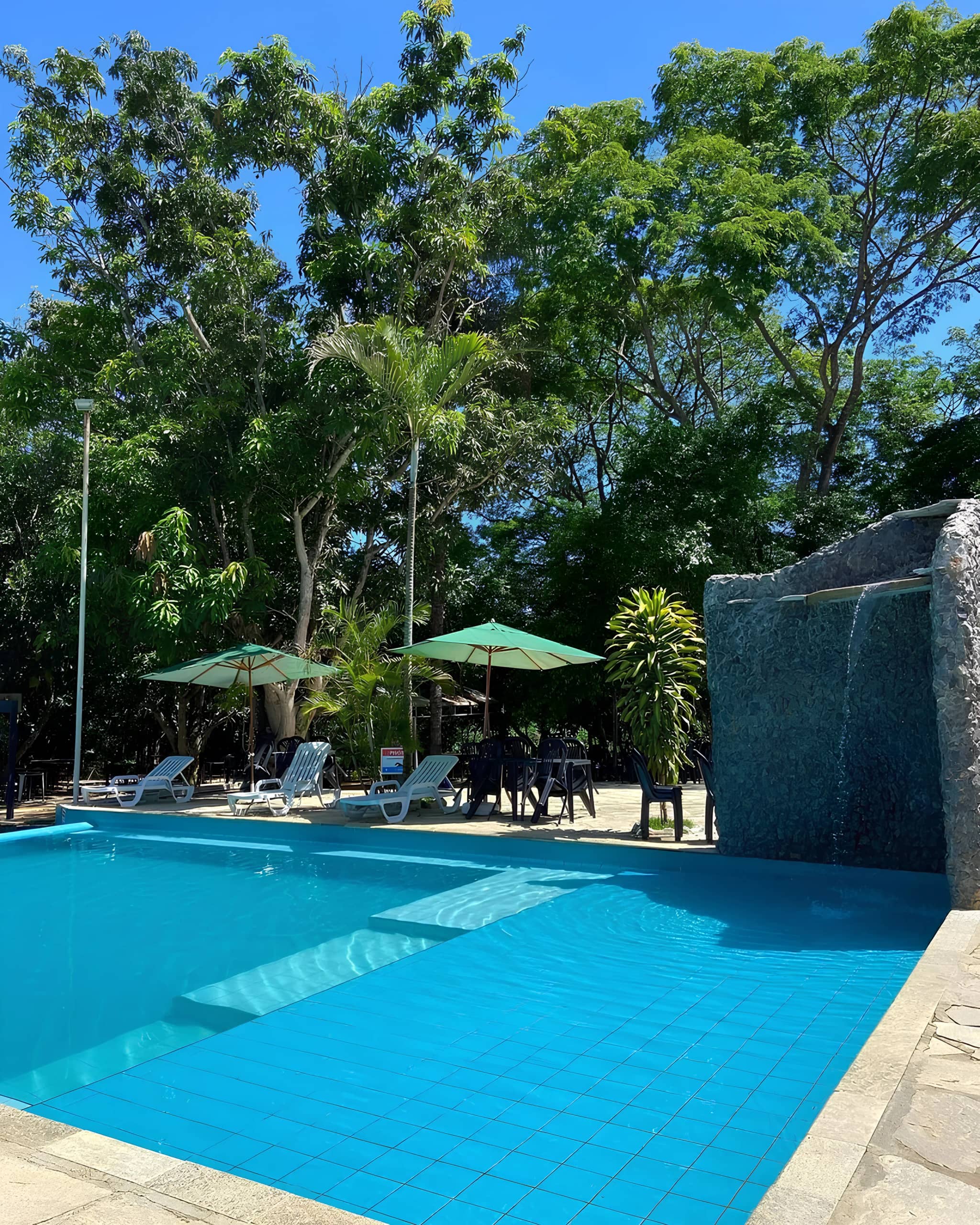 Piscina adulta de água azul com cascata de pedra e guarda-sóis ao redor