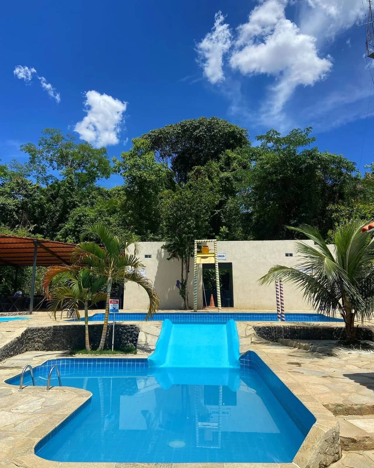 Piscina infantil com escorregador azul e prédio de vestiários ao fundo