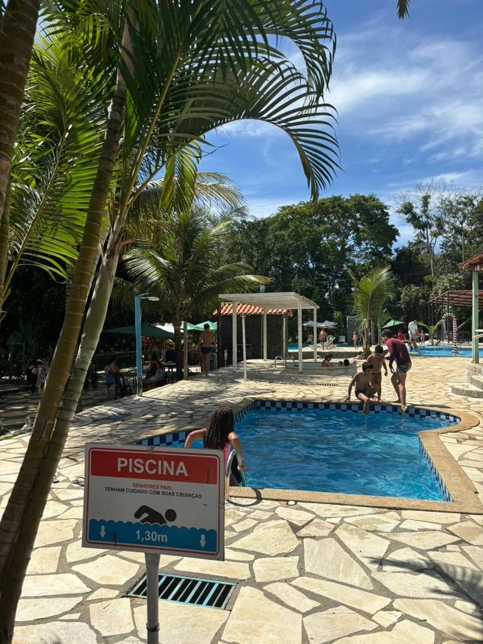 Banhistas na piscina ao lado da placa indicando profundidade de 1,30 metro