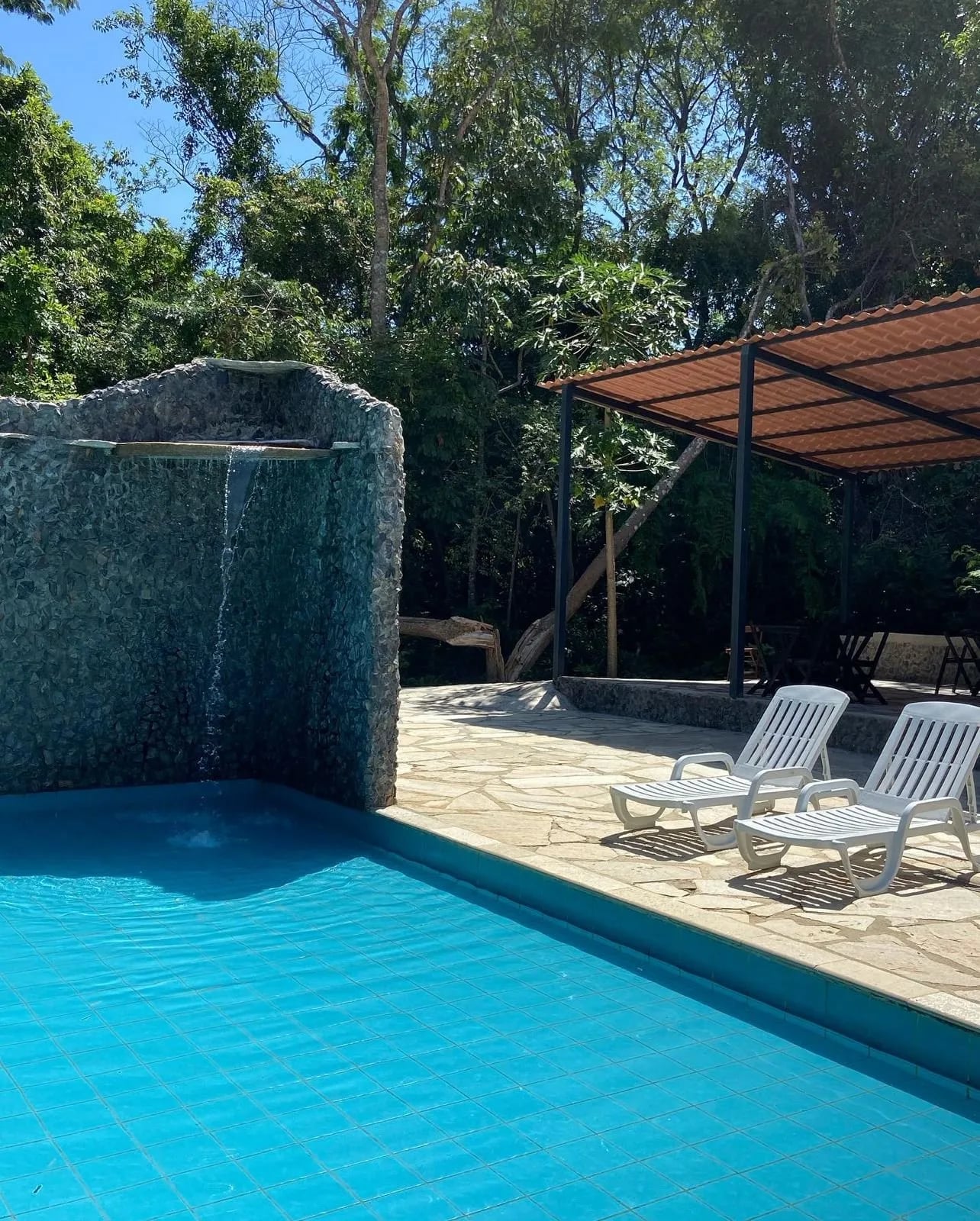 Cascata de pedra caindo na piscina azul com espreguiçadeiras ao sol