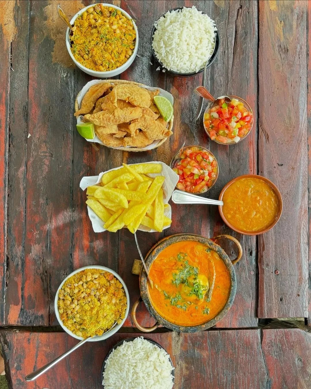 Vista de cima da mesa com peixe frito, batata, tropeiro, arroz e moqueca